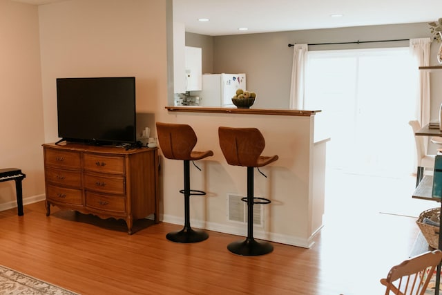 interior space with a kitchen breakfast bar, light wood finished floors, visible vents, and freestanding refrigerator