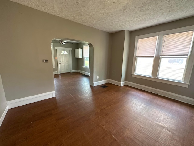 empty room featuring visible vents, arched walkways, baseboards, and dark wood-style floors