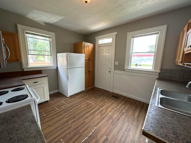 kitchen with white appliances, dark wood-style floors, baseboards, a sink, and a textured ceiling