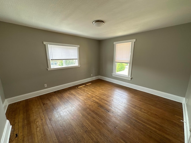 empty room with plenty of natural light, baseboards, and dark wood-style flooring