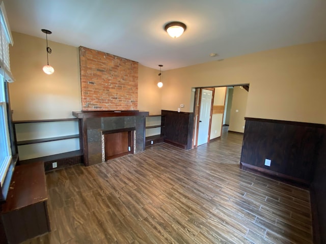 unfurnished living room with a wainscoted wall, a large fireplace, and wood finished floors