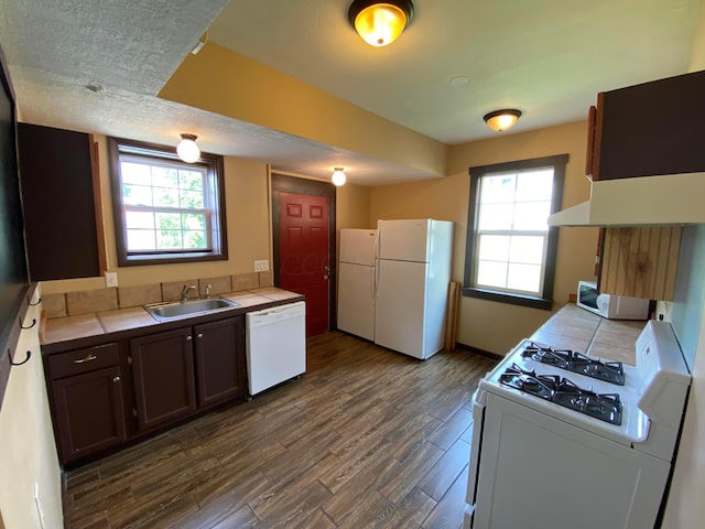 kitchen featuring a wealth of natural light, a sink, dark wood-style floors, tile countertops, and white appliances