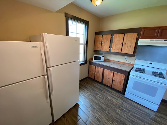 kitchen featuring tile counters, under cabinet range hood, brown cabinets, dark wood-style floors, and white appliances