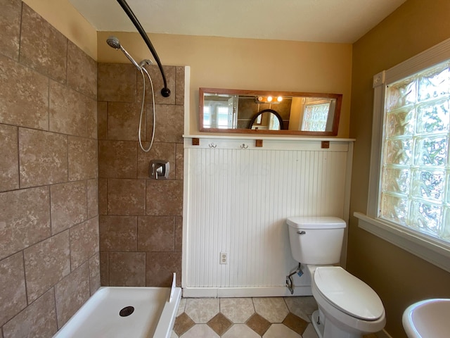 bathroom with toilet, a healthy amount of sunlight, and tiled shower