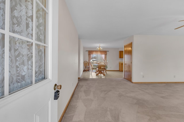 interior space featuring light colored carpet, ceiling fan with notable chandelier, and baseboards