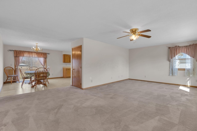 unfurnished living room with ceiling fan with notable chandelier, a wealth of natural light, and light carpet