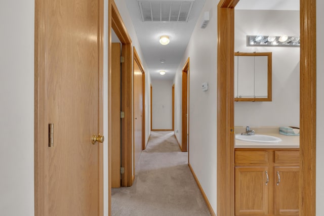 hall with light carpet, baseboards, visible vents, and a sink