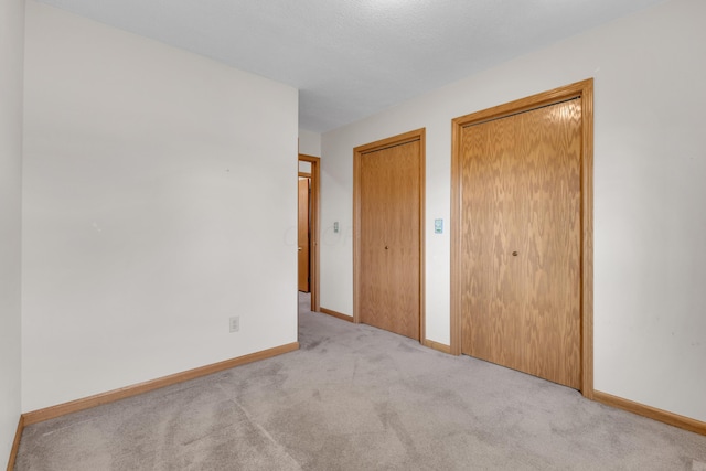 unfurnished bedroom with carpet flooring, baseboards, and multiple closets