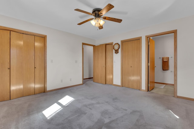 unfurnished bedroom with light colored carpet, baseboards, two closets, and ensuite bath