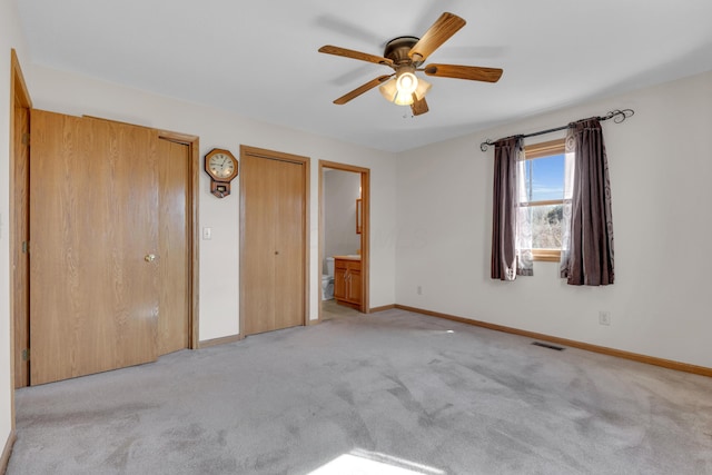 unfurnished bedroom featuring baseboards, visible vents, multiple closets, ensuite bathroom, and light carpet