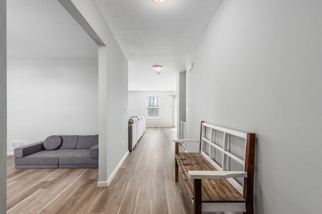 hallway with wood finished floors, visible vents, and baseboards