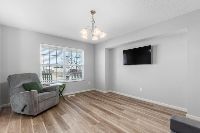 living area with baseboards, light wood finished floors, and a chandelier