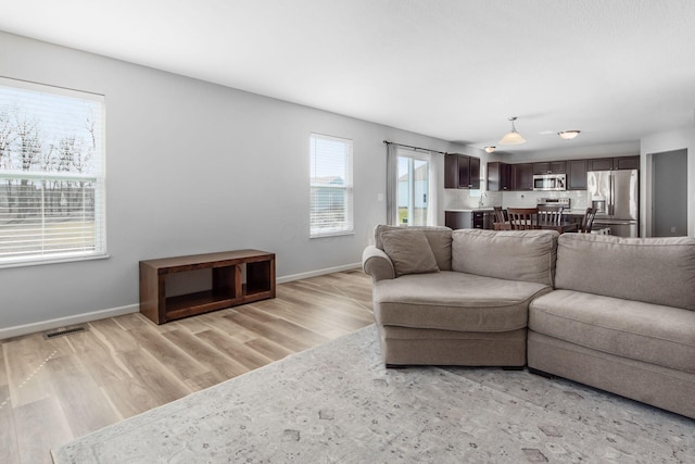 living room featuring visible vents, baseboards, and light wood finished floors