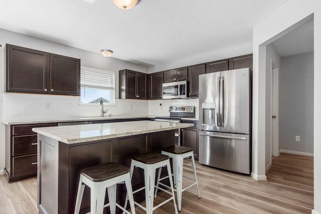 kitchen with dark brown cabinets, light wood-style floors, appliances with stainless steel finishes, and a breakfast bar area