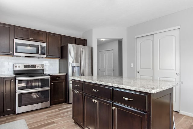 kitchen with light stone countertops, stainless steel appliances, decorative backsplash, dark brown cabinets, and light wood-style floors