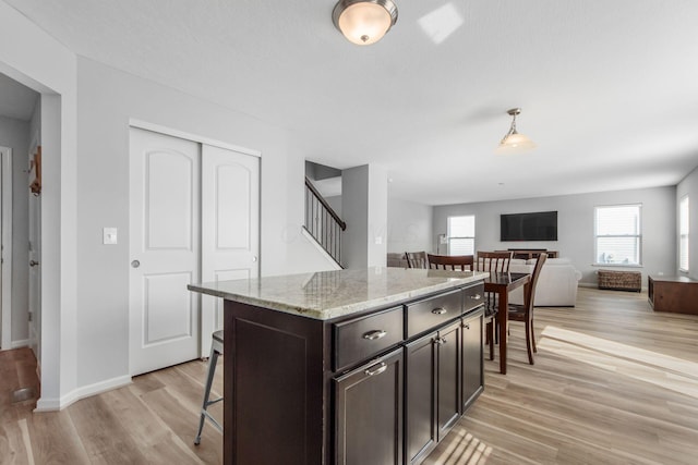 kitchen featuring light stone counters, a kitchen breakfast bar, light wood-style floors, and dark brown cabinetry