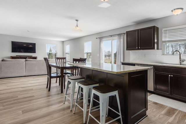 kitchen with a sink, a breakfast bar, decorative backsplash, light wood-style floors, and stainless steel dishwasher