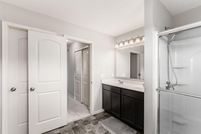 full bath featuring double vanity, baseboards, walk in shower, and a sink