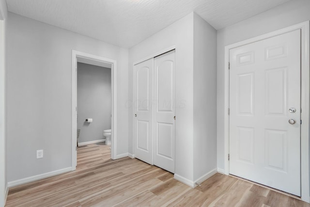 unfurnished bedroom with baseboards, light wood finished floors, a closet, a textured ceiling, and connected bathroom