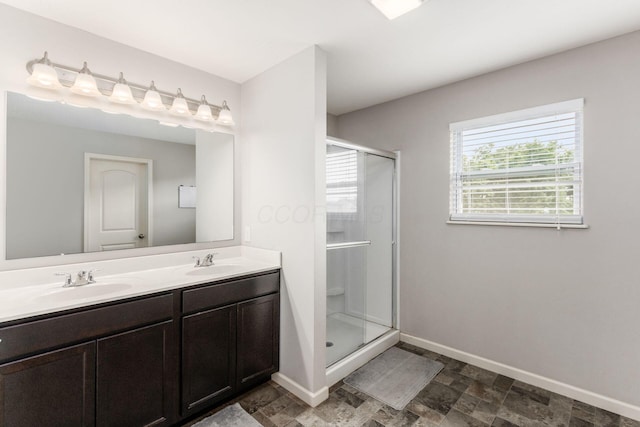 full bathroom featuring double vanity, a shower stall, baseboards, and a sink