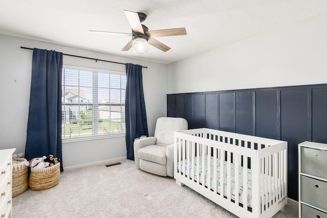 carpeted bedroom with visible vents, a crib, baseboards, and ceiling fan