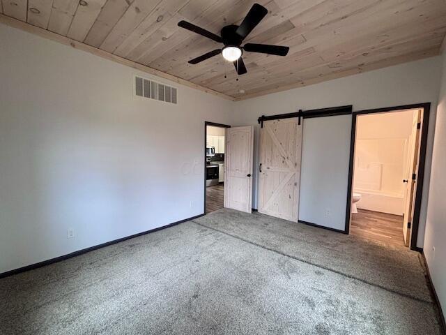 unfurnished bedroom featuring visible vents, carpet floors, wood ceiling, and a barn door