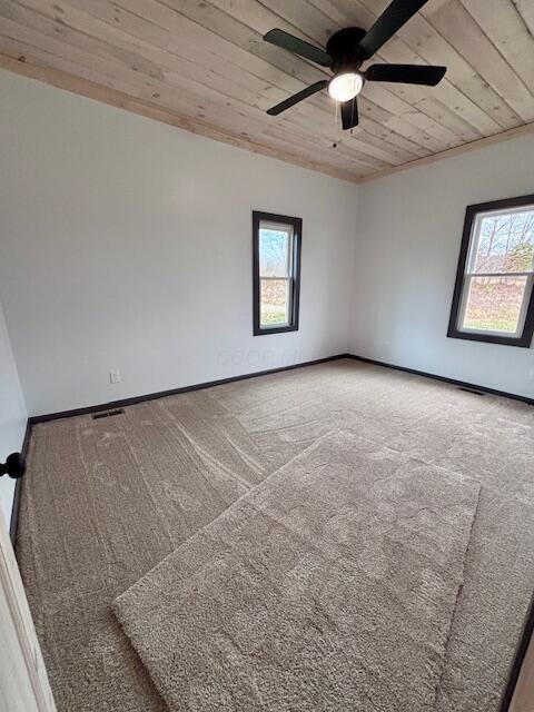 carpeted spare room featuring baseboards, wood ceiling, and a ceiling fan