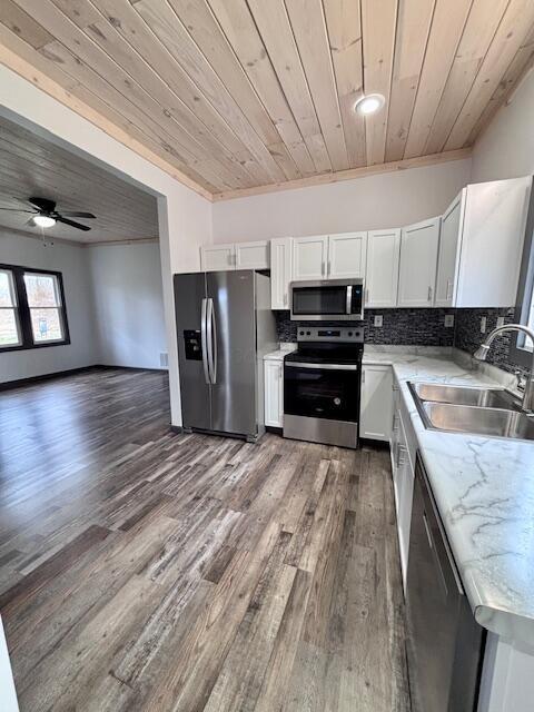 kitchen with a sink, stainless steel appliances, white cabinets, decorative backsplash, and wood ceiling