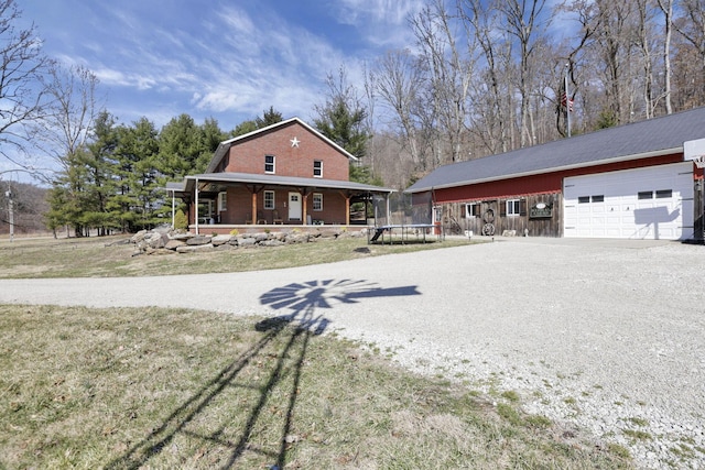 view of front of property with a trampoline, a porch, gravel driveway, an attached garage, and brick siding