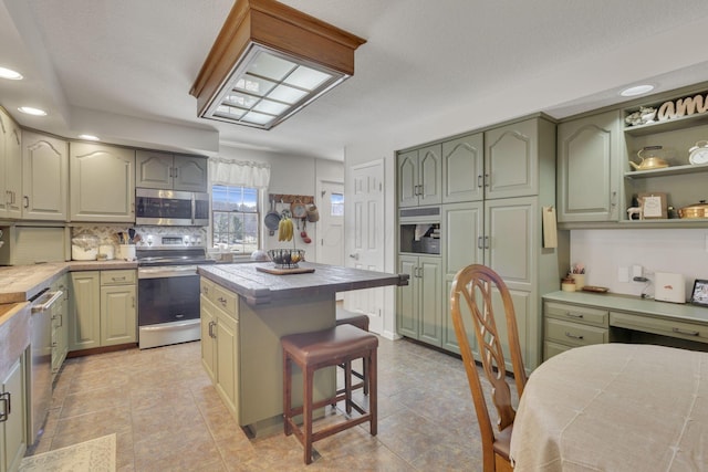 kitchen featuring backsplash, appliances with stainless steel finishes, a breakfast bar area, green cabinetry, and tile counters