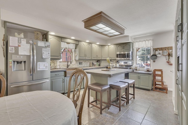 kitchen featuring gray cabinets, tasteful backsplash, a center island, appliances with stainless steel finishes, and light countertops