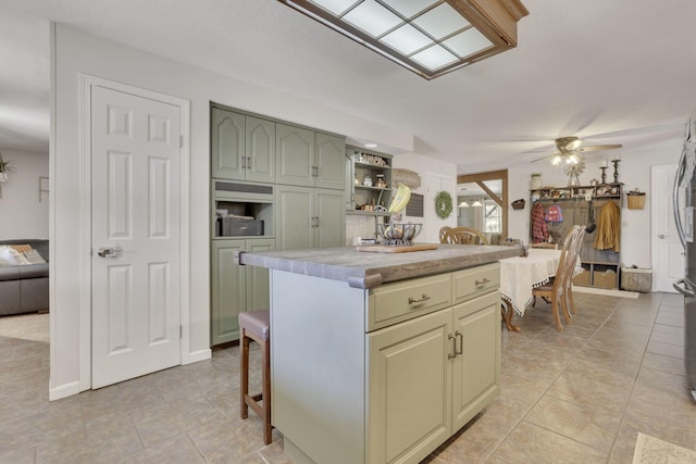 kitchen with light tile patterned floors, green cabinetry, a kitchen island, ceiling fan, and light countertops