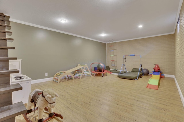 playroom with brick wall, crown molding, baseboards, recessed lighting, and wood finished floors