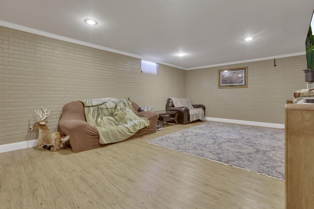 sitting room featuring brick wall, crown molding, baseboards, and wood finished floors