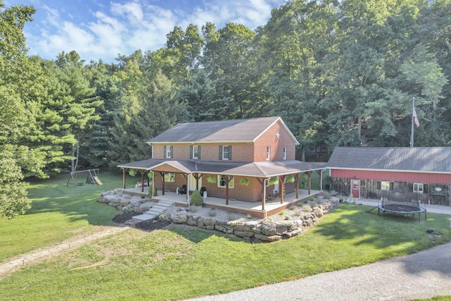 farmhouse-style home with an outbuilding, a front lawn, a trampoline, covered porch, and brick siding