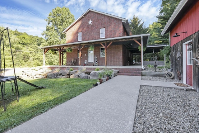 view of front of home featuring a porch, a trampoline, brick siding, and a front lawn