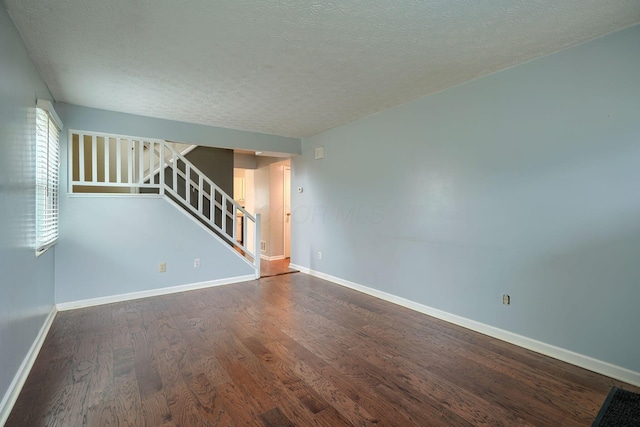 empty room featuring stairs, dark wood-type flooring, baseboards, and a textured ceiling