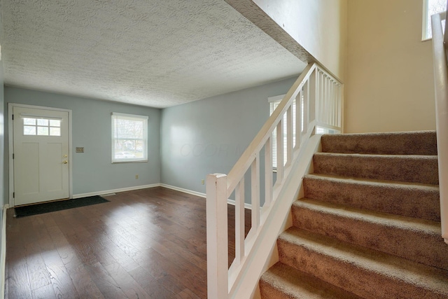 foyer featuring a textured ceiling, stairs, dark wood-type flooring, and baseboards