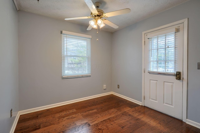 unfurnished room with baseboards, a textured ceiling, a healthy amount of sunlight, and dark wood finished floors