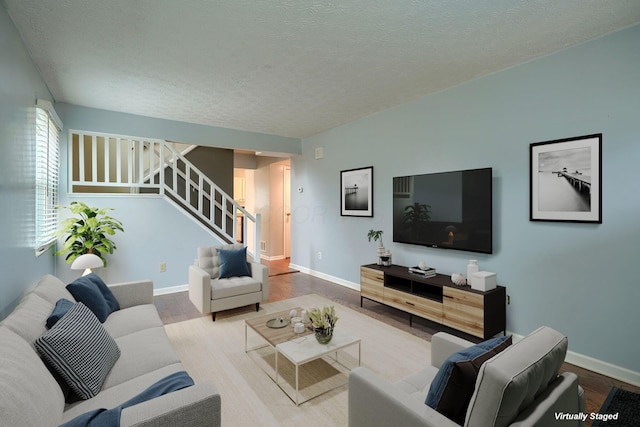 living room featuring stairway, baseboards, a textured ceiling, and wood finished floors