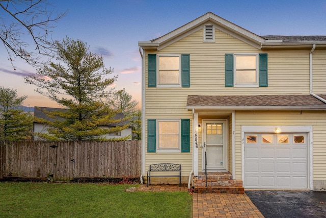 traditional home with fence, aphalt driveway, entry steps, a lawn, and a garage