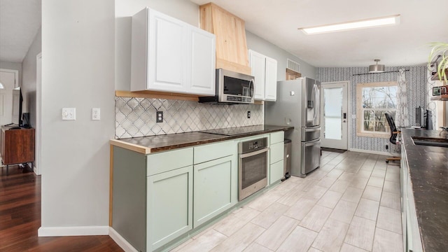 kitchen with a sink, appliances with stainless steel finishes, light wood finished floors, decorative backsplash, and baseboards