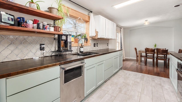 kitchen with a sink, backsplash, wooden counters, white cabinets, and stainless steel dishwasher