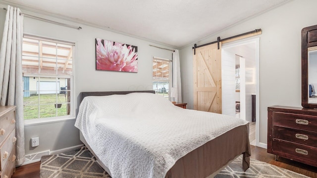 bedroom with a barn door, dark wood-style floors, visible vents, and baseboards