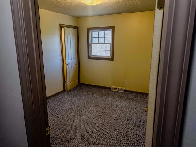 unfurnished bedroom with visible vents, baseboards, a textured ceiling, and dark carpet