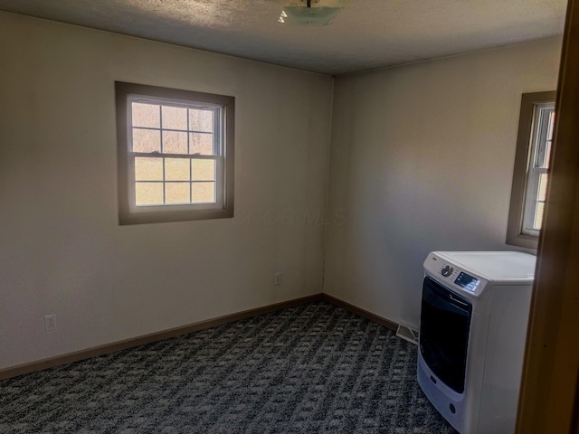 empty room featuring washer / dryer, a textured ceiling, baseboards, and dark colored carpet