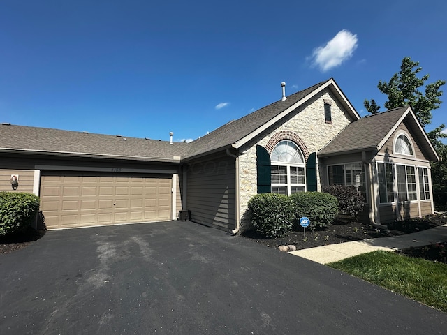 4163 Windbud Dr, New Albany, OH 43054 - ranch-style home featuring asphalt driveway, a garage, stone siding, a sunroom, and roof with shingles