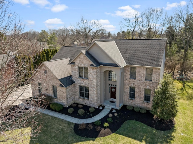 view of front of property featuring a front yard, brick siding, and roof with shingles