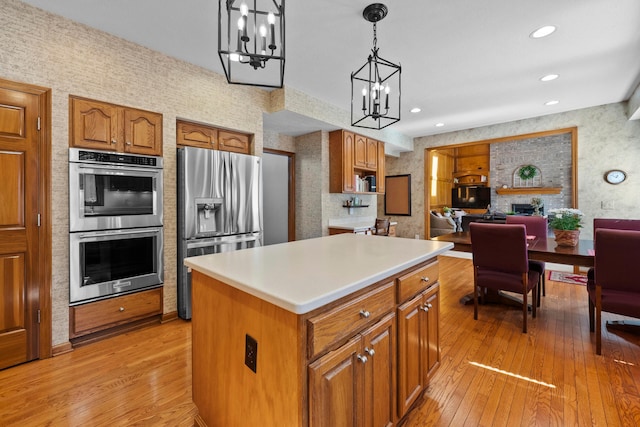 kitchen with light wood-style flooring, an inviting chandelier, appliances with stainless steel finishes, brown cabinetry, and wallpapered walls