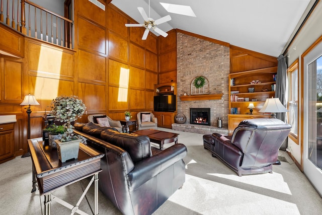 living room with wood walls, light carpet, a fireplace, a skylight, and a ceiling fan